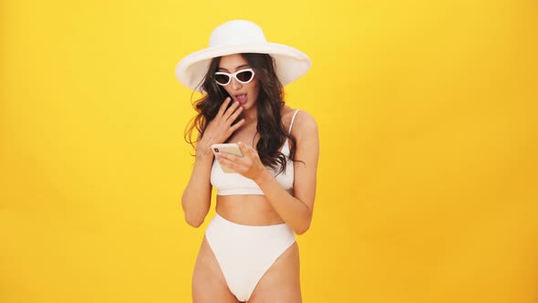 A happy brunette woman wearing a swimsuit doing winner gesture using her mobile