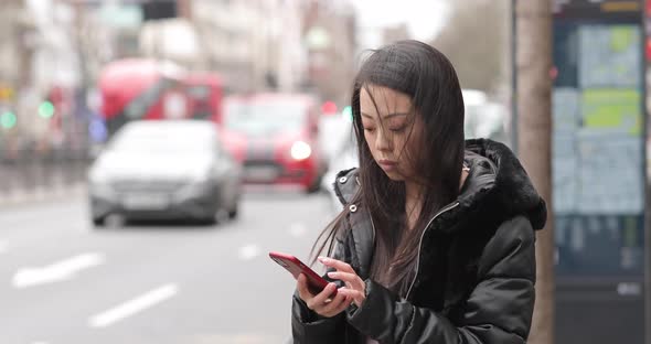Chinese woman waiting at bus stop, using smartphone