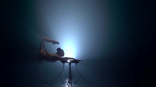 Acrobat on the Table Shows the Tricks of Standing on Her Hands . Smoke Background. Slow Motion