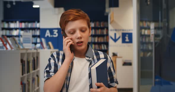 Teen Schoolboy Walking in School Library and Talking on Smartphone