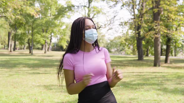 A Young Black Woman in a Face Mask Dances in a Park on a Sunny Day