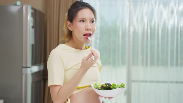 Asian beautiful pregnant woman eating healthy food in kitchen at home.