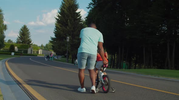 Rear View of Caring Dad Helping Son To Ride Bike