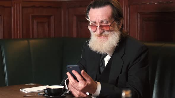 Senior Stylish Man Sitting in Pub and Using His Phone