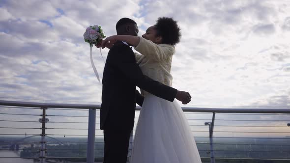 Happy Smiling African American Bride Hugging Groom Standing on Bridge Outdoors