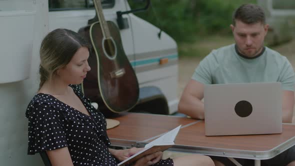 Traveler Man working at laptop and woman reading the book in summer camping.