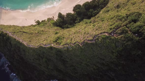 Aerial overhead view of Kelingking Beach in Nusa Penida, Bali, Indonesia. People go down the path to