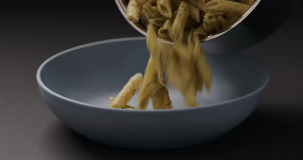 Slow Motion Pesto Penne Fall Into Blue Bowl on Black Background