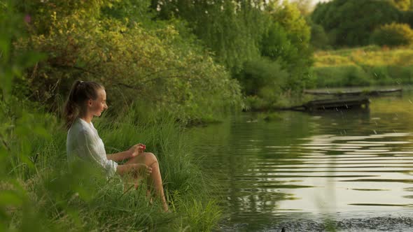 Young Woman Sitting on Dock Splashing Bare Legs in Lake