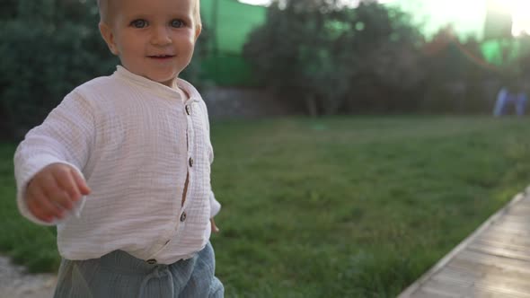 Cute Little Boy in White Shirt Walks in Yard at Sunlight