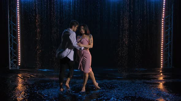 Loving Couple Passionately Dances Against the Background of the Rain in a Dark Studio