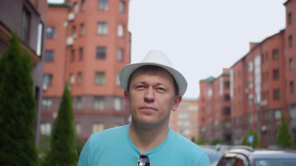 Male tourist in a hat walks around the city, tracking with a camera