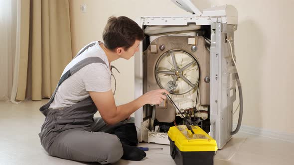 Master Opens Back Panel of Broken Washing Machine Near Wall