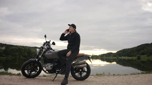 Motorbike Driver Talking on His Phone Sitting on a Scrambler By Lake in Autumn