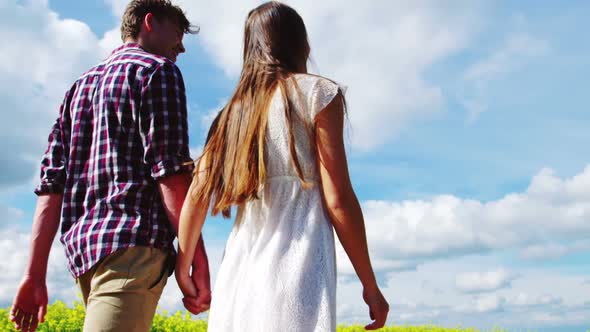 Romantic couple holding hands while walking in field