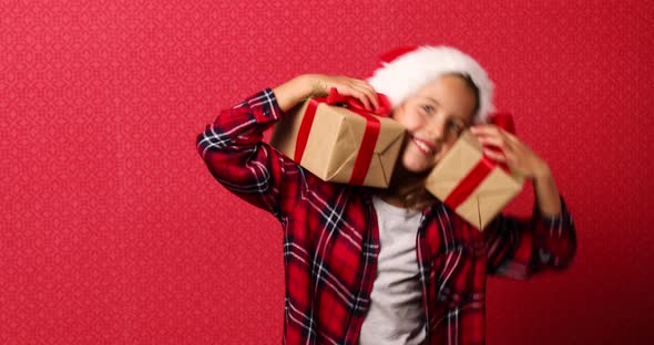 Surprised and Positive little girl in santa hat holding two Christmas presents, gift boxes,