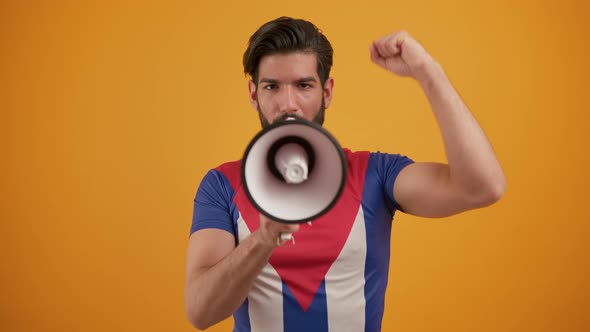 Medium Studio Shot Over an Orange Background of a Confident Latino Guy in a Cuban Flag Tshirt