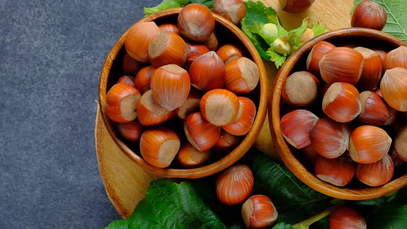 Hazelnuts in a wooden bowl set with leaves on a wooden saw cut on a black slate background