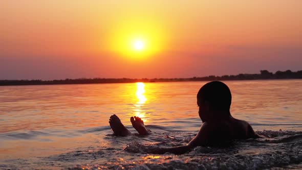Silhouette of Boy Sitting in the Water on Background of Sunset and Orange Path. Slow Motion