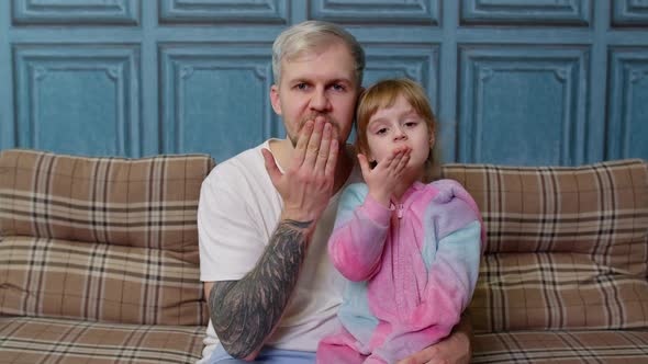 Father and Child Daughter Girl in Pajamas Sit on Couch in Room Smiling Blowing Sending an Air Kiss