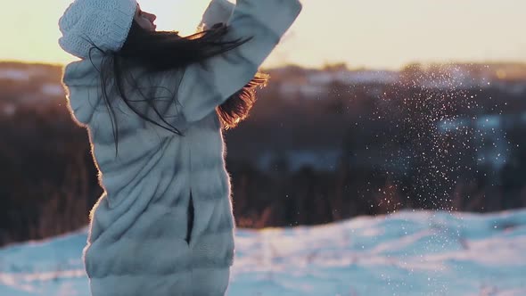 Young Pretty Smiling Woman Throws Snow Lit By Evening Sun