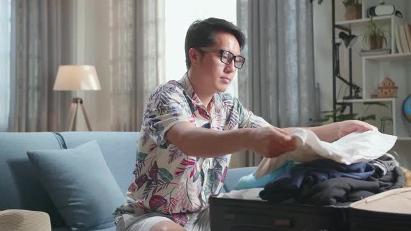 Asian Young Man Packing Clothes In Suitcase At Home, Preparing For Vacation