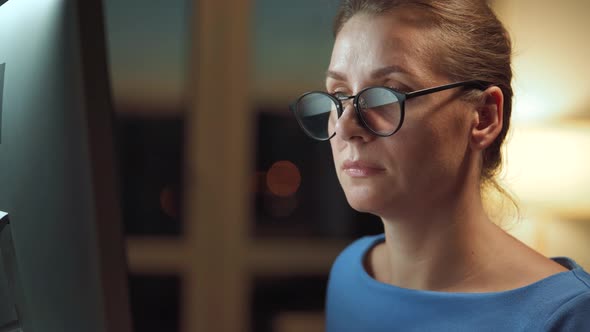 Woman in Glasses Looking on the Monitor and Surfing Internet. The Monitor Screen Is Reflected