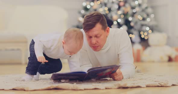 Kid with Dad Spends Time Reading a Book While Lying on the Carpet, Cozy Winter Evening at the New