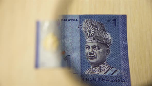 One Malaysian ringgit and magnifying glass.