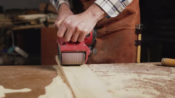 Carpenter Sanding Wood with Belt Sander at Workshop in Wooden Board Project or Woodworking Carpentry
