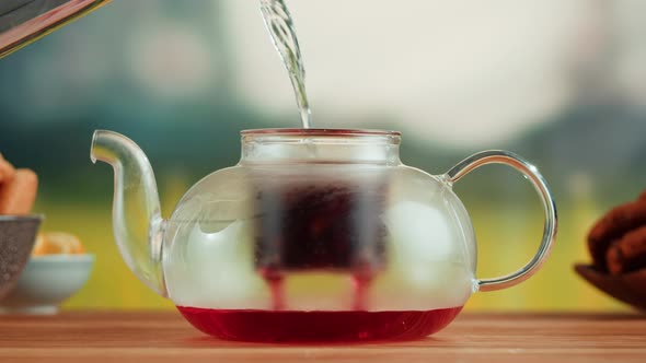 Pouring Hot Water Into Teapot with Red Fruit Tea on a Wooden Table