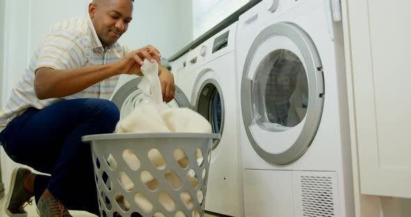 Side view of mid adult black man washing clothes in washing machine at comfortable home 4k