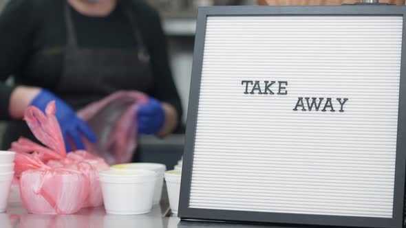 Take Away Announcement Closeup with Blurred Woman Packing Food Containers with Donations for