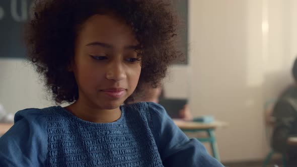 Cheerful African American Girl Sitting at Desk with Tablet Computer in School