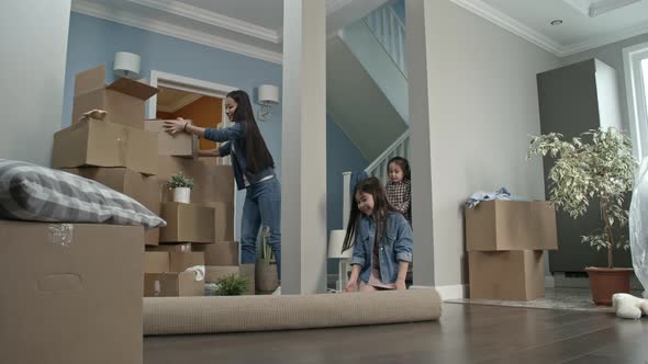 Mother and Children Unrolling Carpet in New House