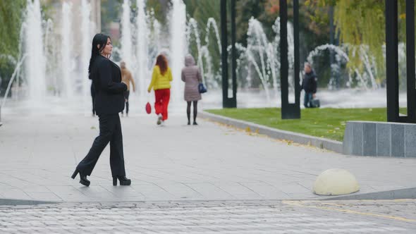 Hispanic Brunette Girl Walks in Park at Lunchtime Walking Slowly Down Street Near the Carriageway on