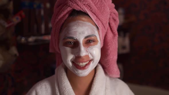 Beautiful Woman with a Towel on Her Head with Facial Mask in Bathroom