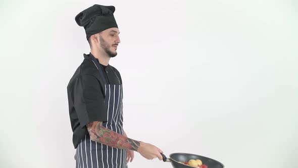 Young Male Chef Flipping Vegetables in Wok in Slow Motion Against White Background