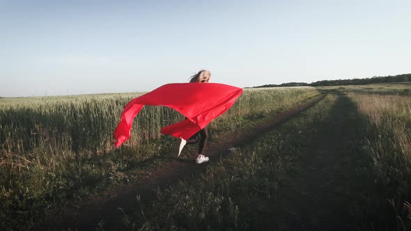 Young Girl Running with Red Tissue in Green Field. Happy Cute Girl Playing in the Wheat Field on a