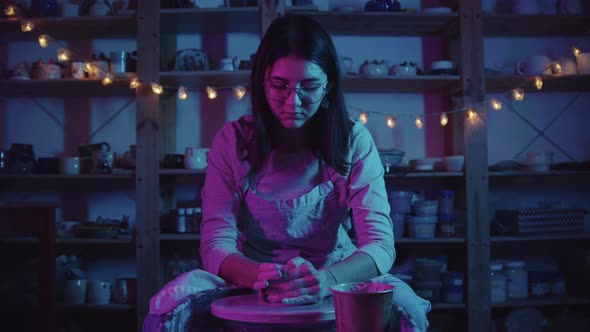 Young Woman Potter in Glasses Working in the Studio in Neon Lighting