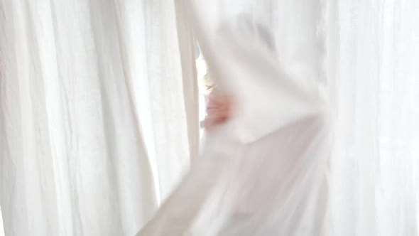 Joyful Girl in Pajamas Hides Behind White Curtain in Room