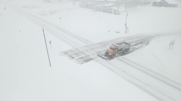 Snowplow clearing highway intersection during snowstorm for rural neighborhood. alt