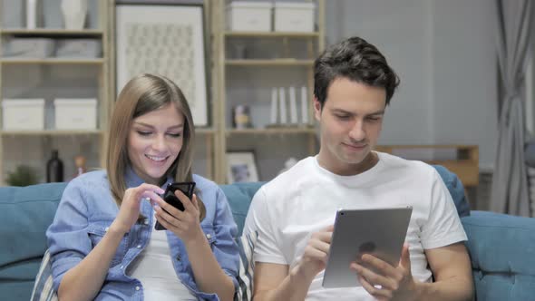 Young Couple Using Smartphone and Tablet While Relaxing on Couch