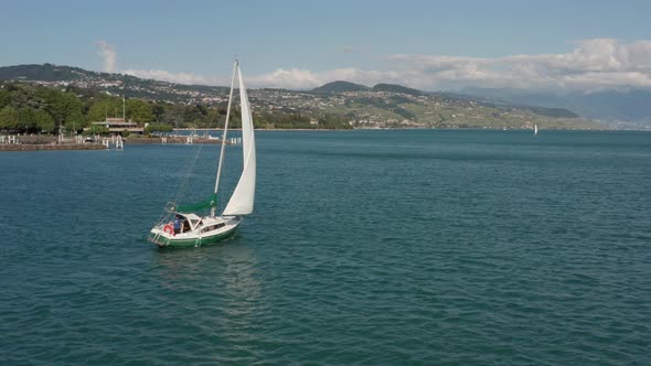 Beautiful aerial of boat sailing over lake Geneva and slowly revealing a large city in the backgroun