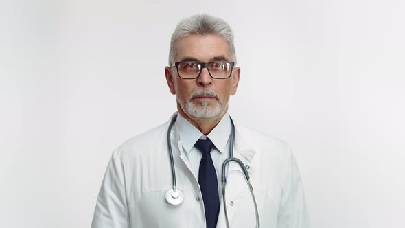 In Studio Doctor in a Uniform with Stethoscope and Glasses Looks Into the Camera and Crosses Arms