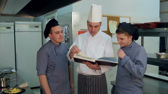 Young Cook Trainees Having Positive Discussion with Chef Holding Cookbook