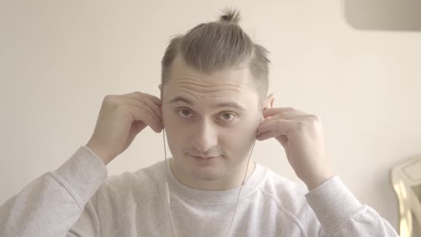 Portrait of Young Caucasian Man Putting on Earphones and Greeting Someone in Video Chat. Close-up of