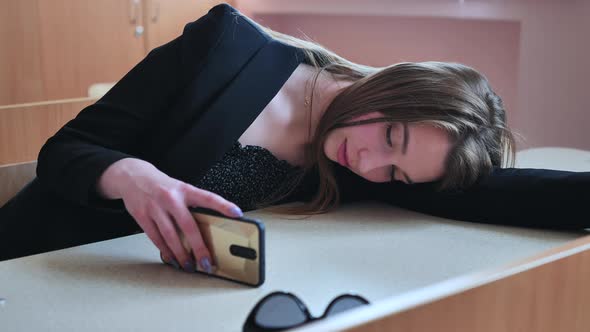 A Tired Student Lying on Her Desk Looks at Her Smartphone and Then Smiles