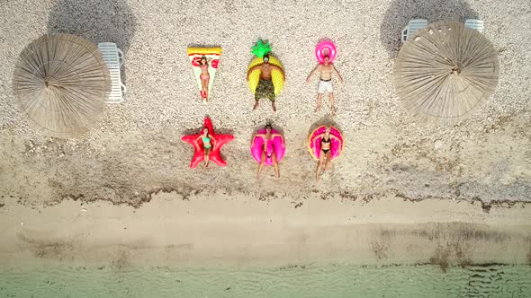 Aerial view of people lying on big inflatable mattresses on beach.