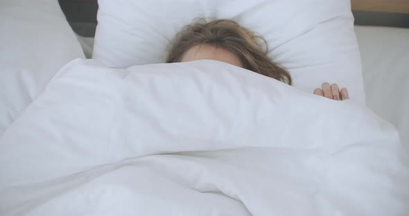 Happy Woman Peeking Out From Her Blanket in Bed and Smiling. Peeking Under Duvet and Smiling